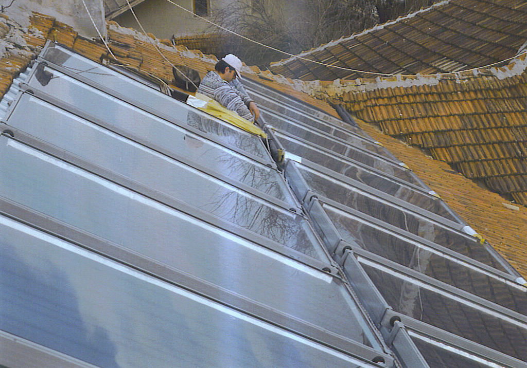 Работник с бяла предпазна каска монтира слънчева инсталация на покрива на къща.